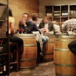 Lively bar setting with people enjoying drinks and tapas around wine barrel tables.